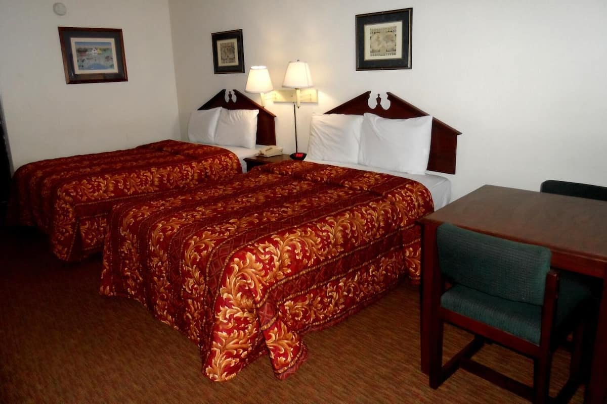 A hotel room with two beds, a desk, and a chair. There are two bedside tables with lamps.
