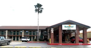 A Budgettel Inn with a brick facade, a palm tree, and a parking lot with several vehicles.