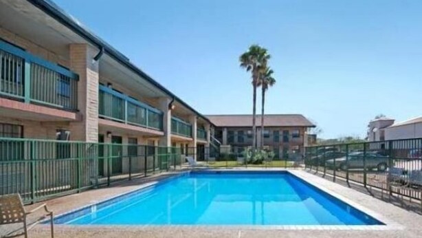 A hotel with a swimming pool, a palm tree, and a clear blue sky. - Budgetel Inn NASA (Houston)