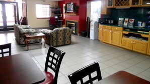 A living room with a sofa, a dining table with chairs, a kitchen area with wooden cabinets, and a television on the wall. - Budgetel Inn NASA (Houston)
