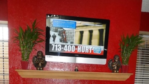 A red wall with a mounted television displaying an advertisement for a 713-400-HURT service. - Budgetel Inn NASA (Houston)