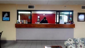 A reception area with a wooden reception desk, a clock, and a wall-mounted television. - Budgetel Inn NASA (Houston)