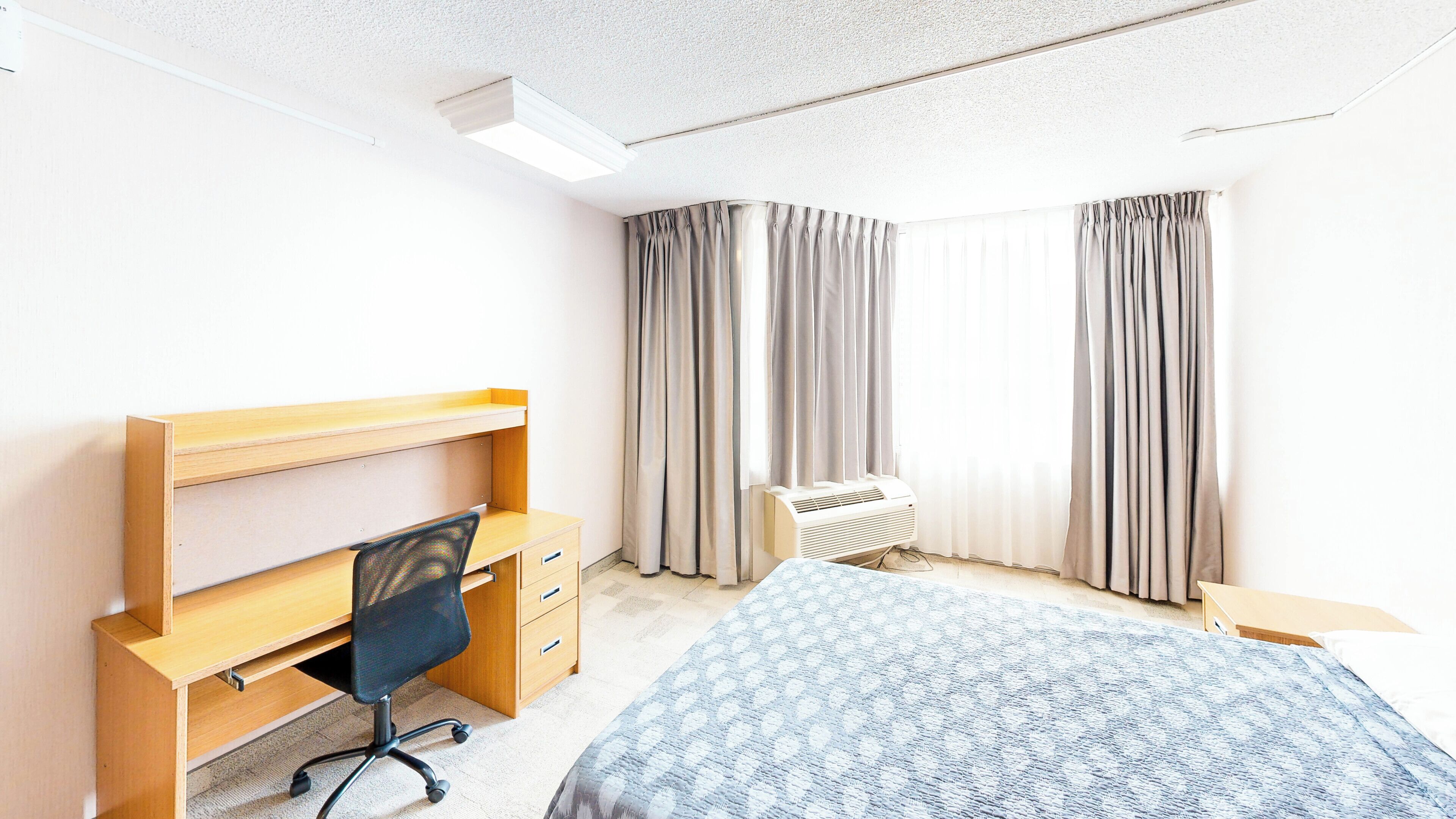 Une chambre à coucher avec un lit, un bureau et une chaise, un radiateur et des rideaux.
