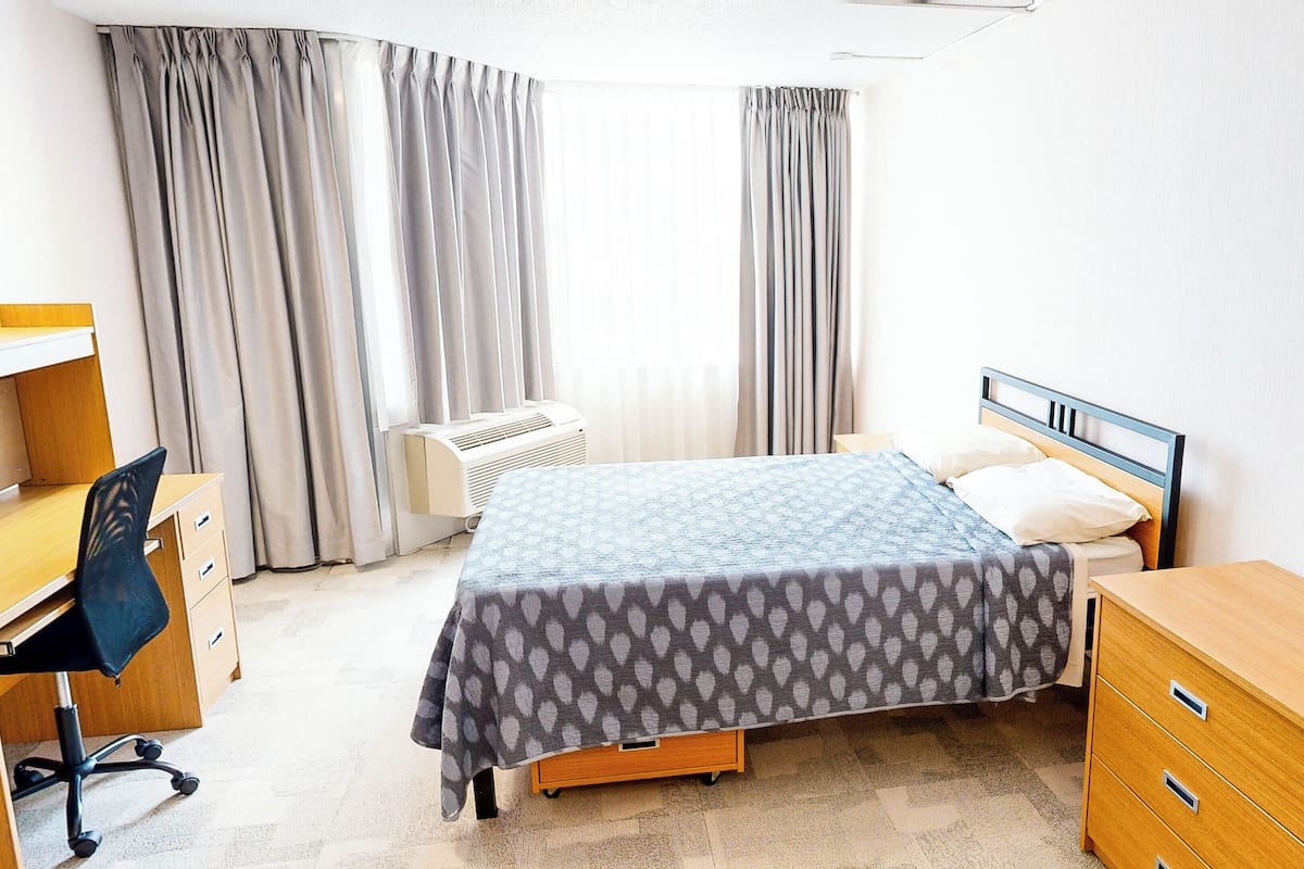 Ein Schlafzimmer mit Bett, Schreibtisch, Stuhl, Kommode und Klimaanlage.