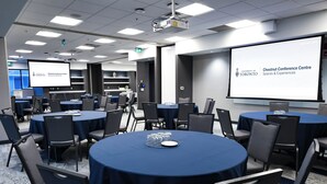 Une salle de conférence équipée de tables rondes, de chaises et d’un écran de projection affichant une image du centre de conférences Chestnut de l’Université de Toronto.