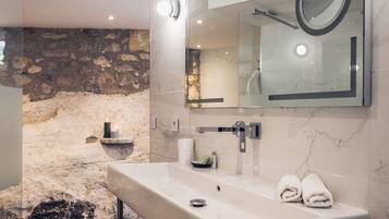 Un baño moderno con pared de piedra, un espejo grande, un lavamanos con toalla y un box de ducha de vidrio.