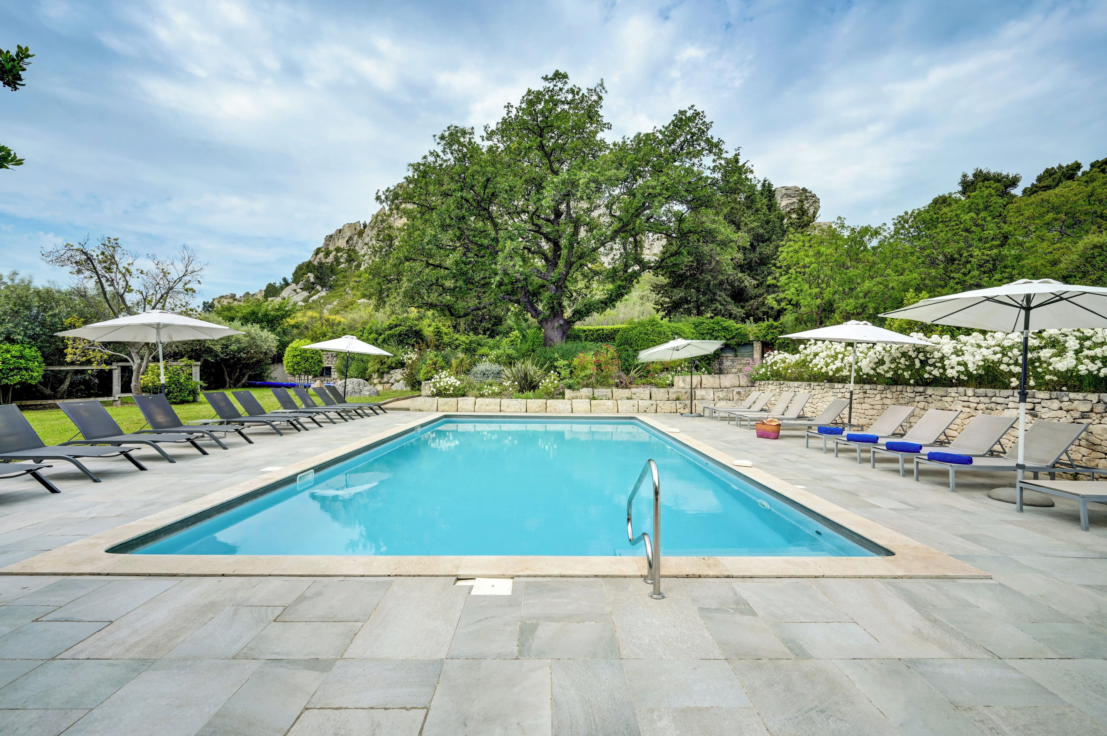 A rectangular swimming pool with a metal ladder, surrounded by lounge chairs and umbrellas.