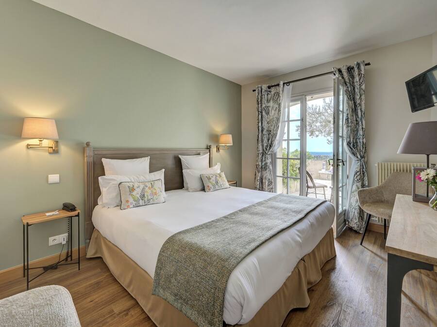 A well-lit bedroom with a large bed, bedside lamps, a desk with a chair, and a view through a window.