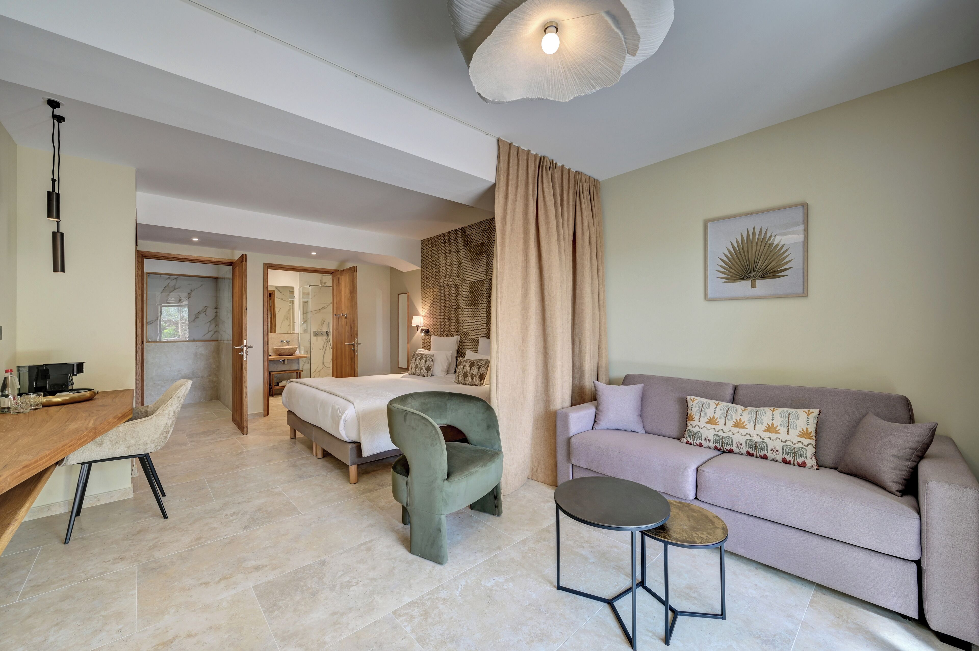 A modern hotel room with a bed, a sofa, a chair, a small table, and a desk with a chair.