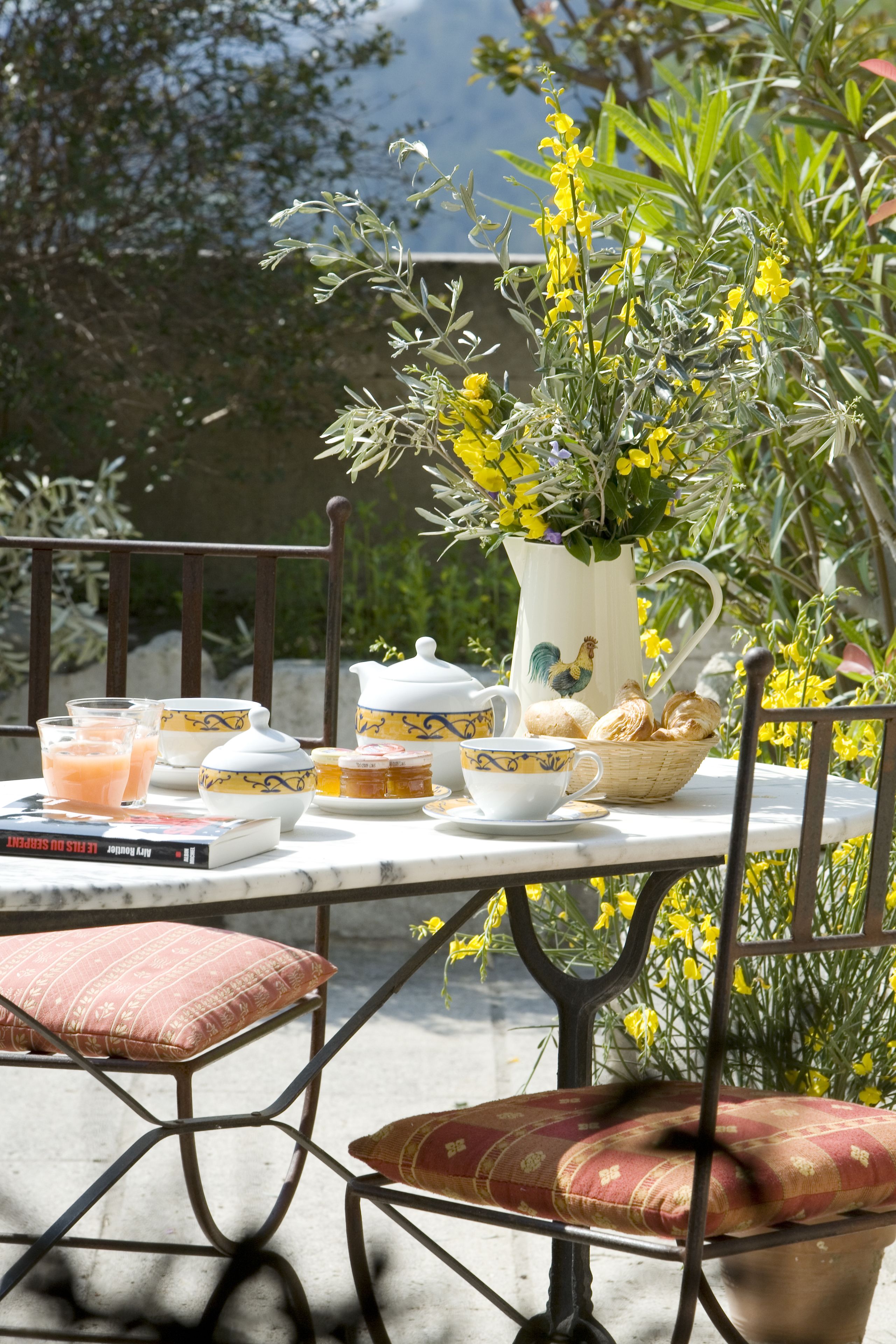 A table set outdoors with a pitcher, teapot, cups, and pastries.
