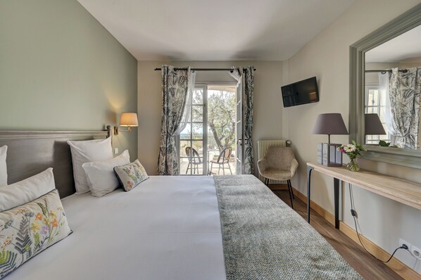 A hotel room with a bed, a desk, a chair, a TV, and a view of the outdoors.