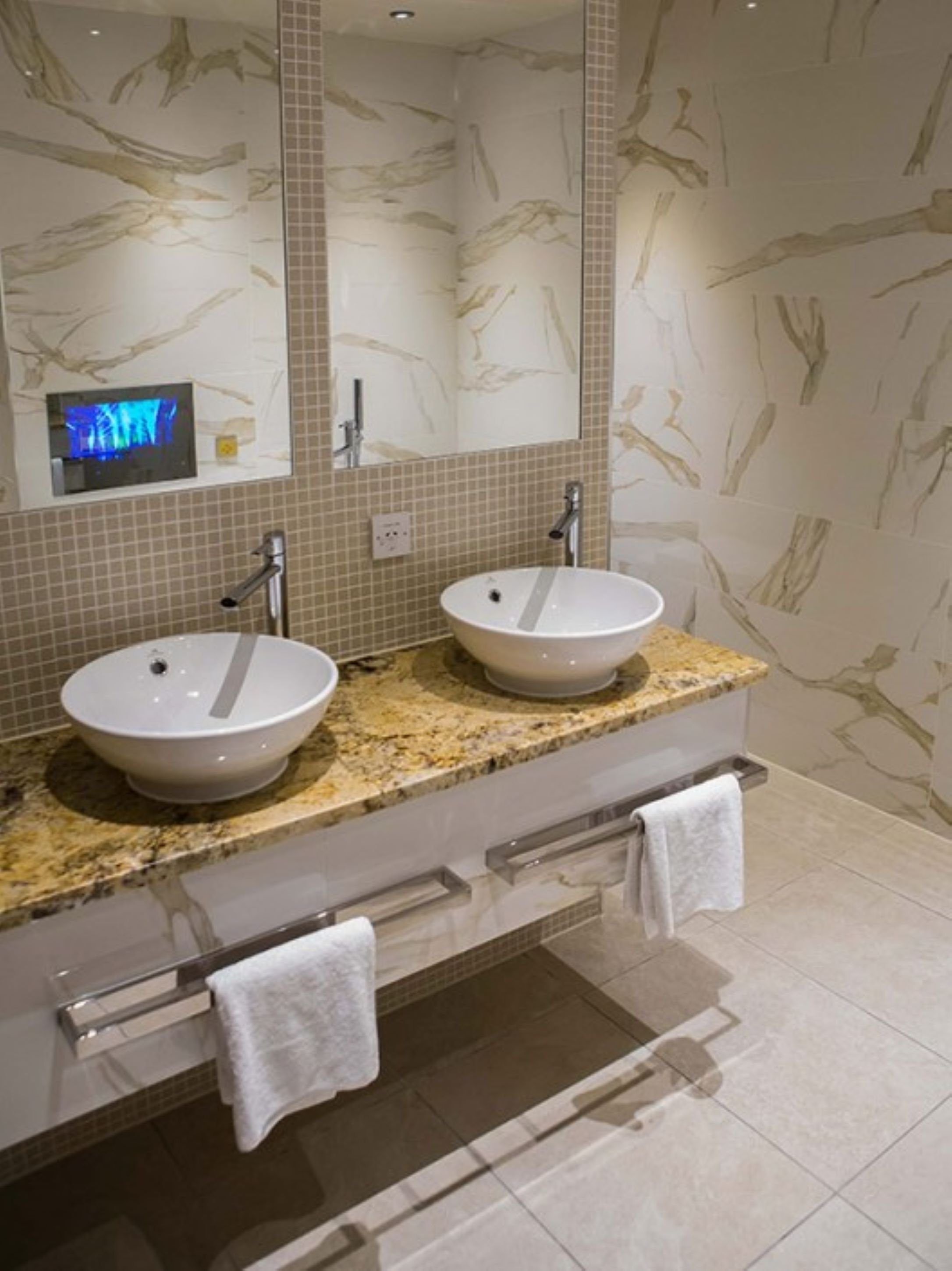 A bathroom with two sinks, a large mirror, and a television above the left sink.