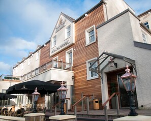 A hotel with a wooden facade, a balcony with outdoor seating, and classic street lamps. - The Busby Hotel (Glasgow)