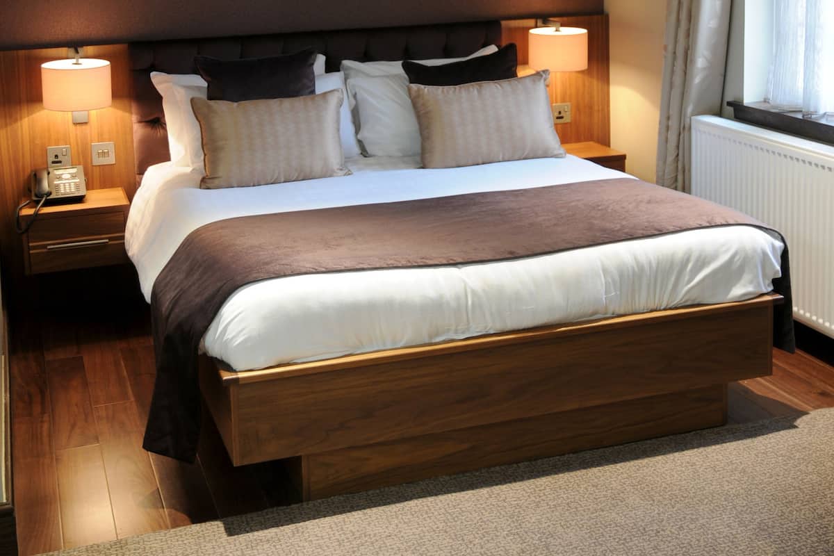 A neatly made bed with a wooden headboard, two bedside lamps, and a window with curtains.