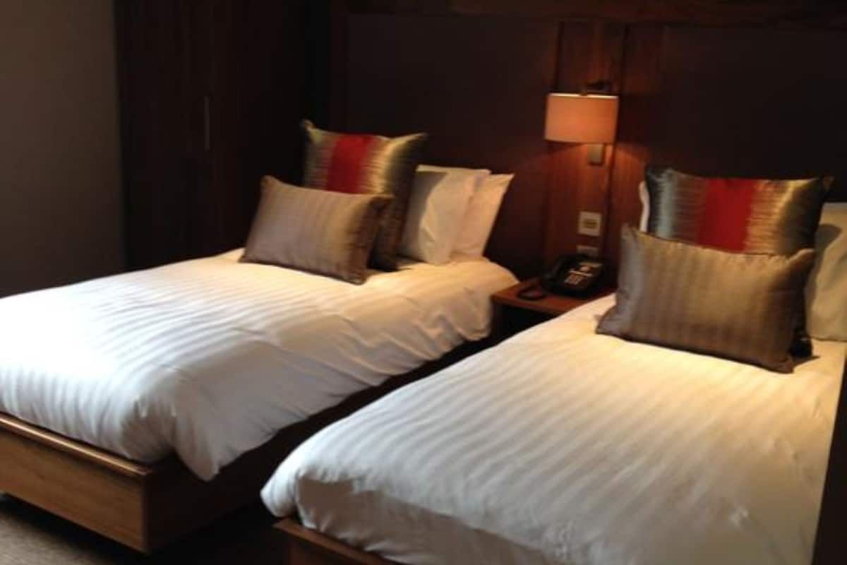 A hotel room with two single beds, a wooden headboard, a nightstand with a lamp, and a carpeted floor.