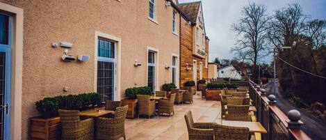 A building with a brick exterior, multiple windows, and outdoor seating with wicker furniture.
