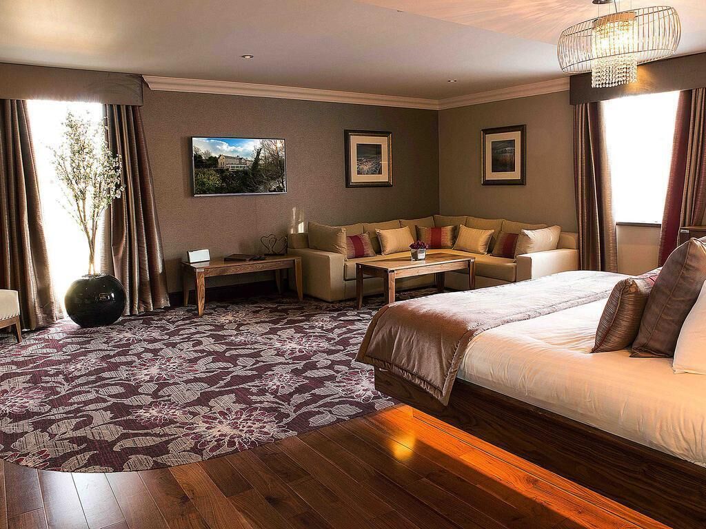 Una habitación de hotel con una cama, un sofá, una mesita y un jarrón grande.