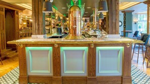 Una zona de bar con mostrador central, paneles de madera y luces colgantes.