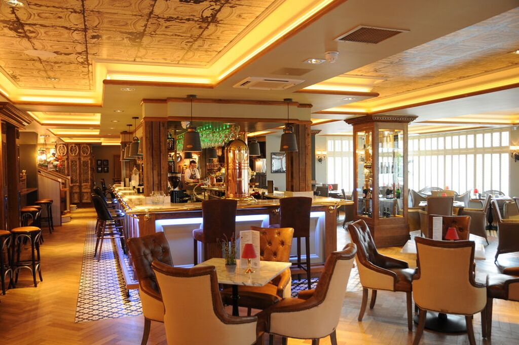 Una zona de bar con una barra alargada, taburetes y un barista detrás de la barra.