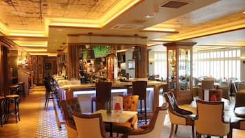 Una zona de bar con una barra alargada, taburetes y un barista detrás de la barra.