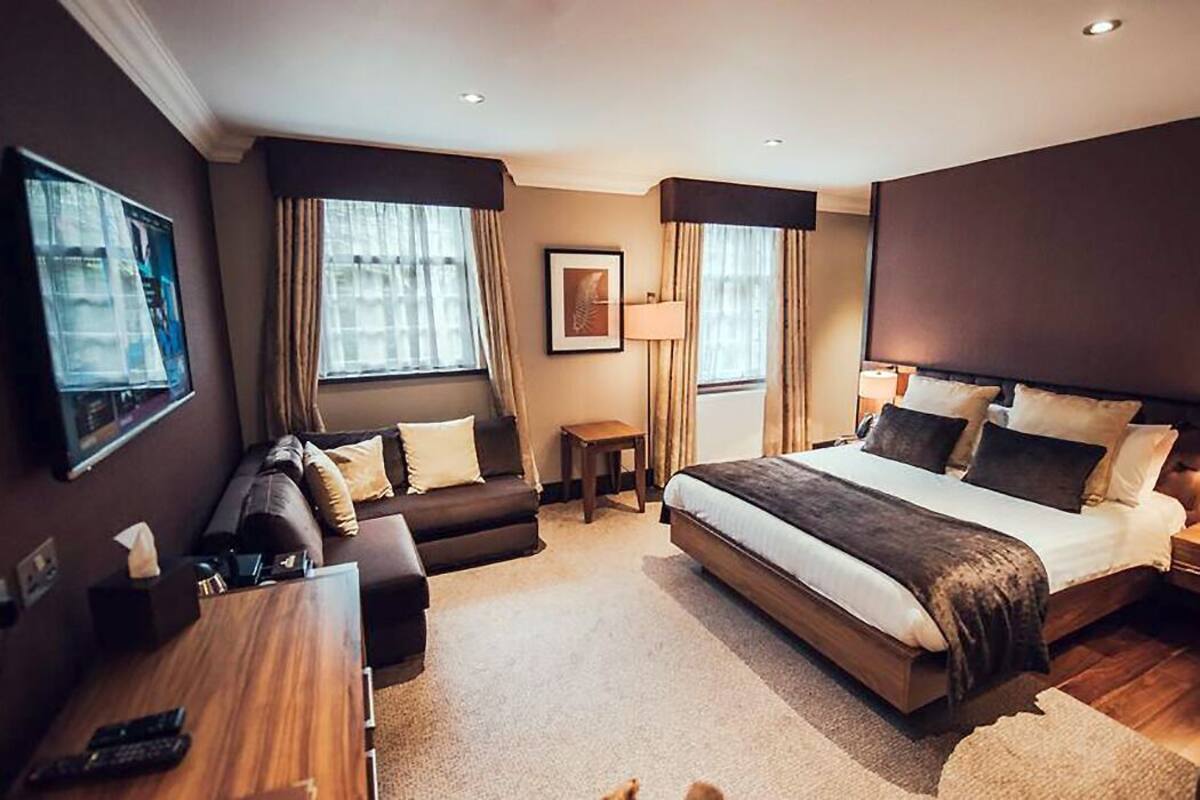A hotel room with a bed, a sofa, a small table, and a TV on the wall.