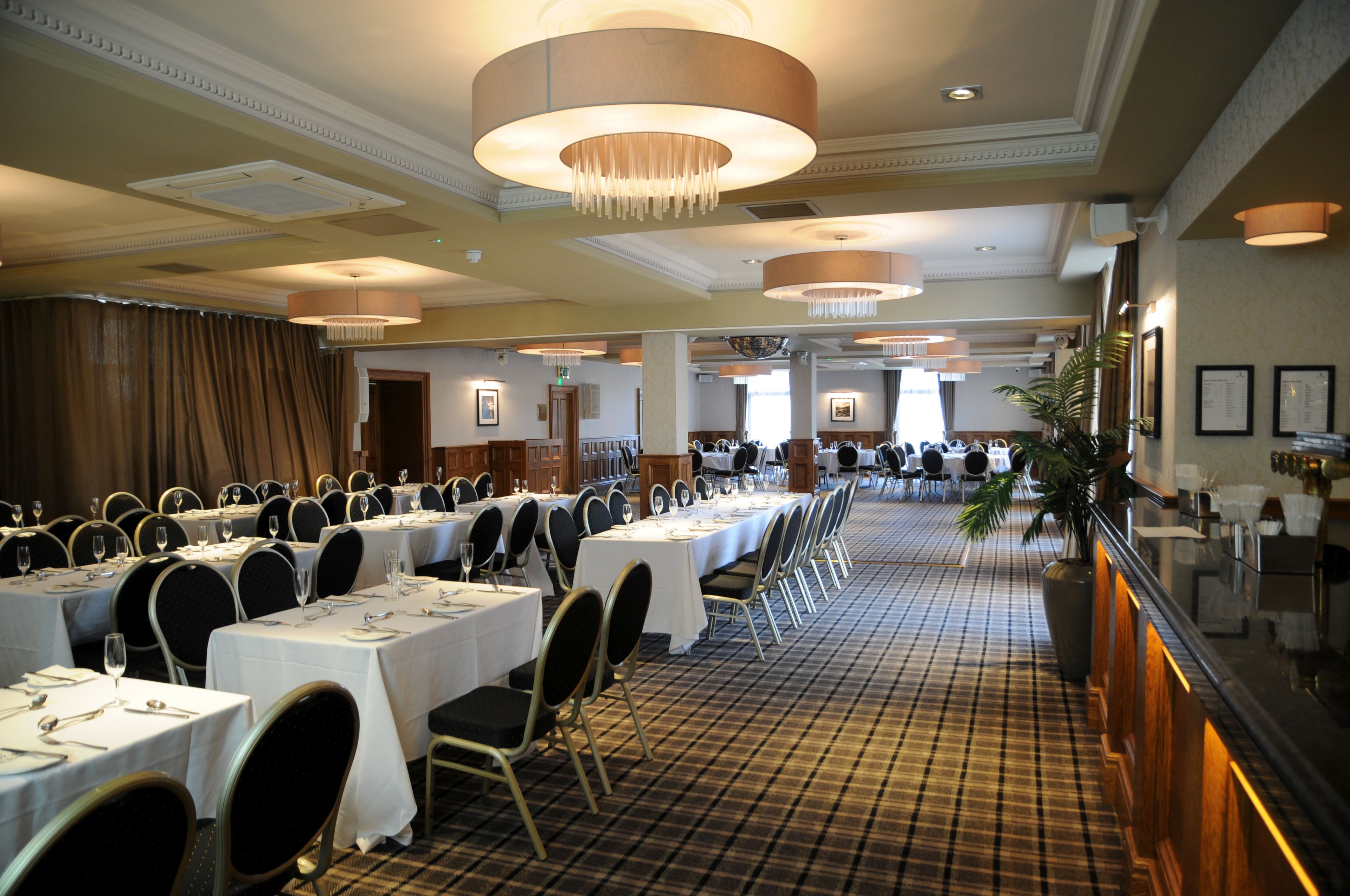 A banquet hall with rows of tables set for dining, a checkered floor, and a chandelier.