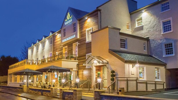 Un hotel de varios pisos con un letrero llamativo, asientos al aire libre y una entrada bien iluminada.