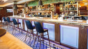 Una zona de bar con una barra larga, varios taburetes y una gran variedad de botellas y vasos en estantes.