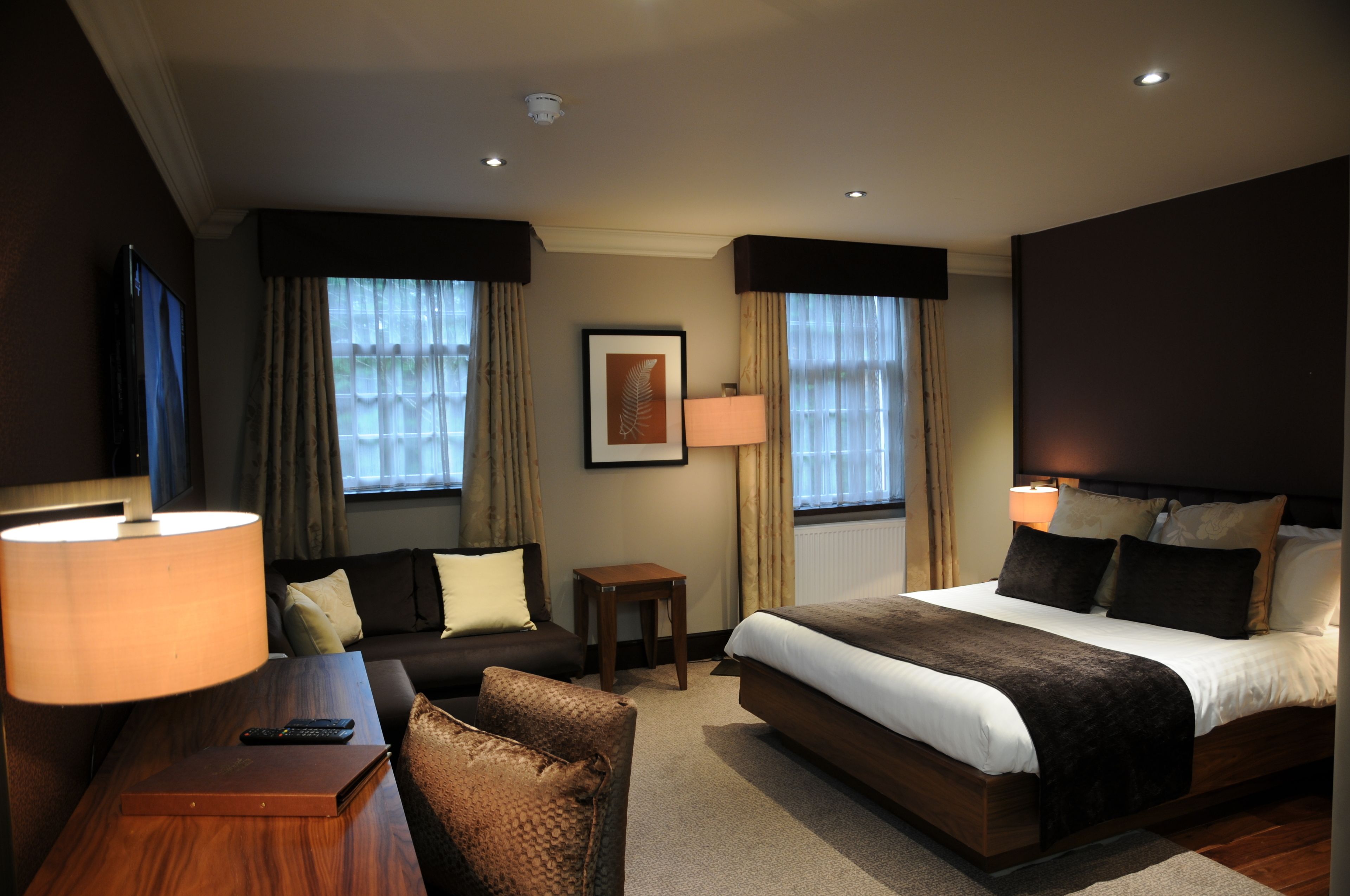 A hotel room with a bed, a sofa, a desk, and a lamp.