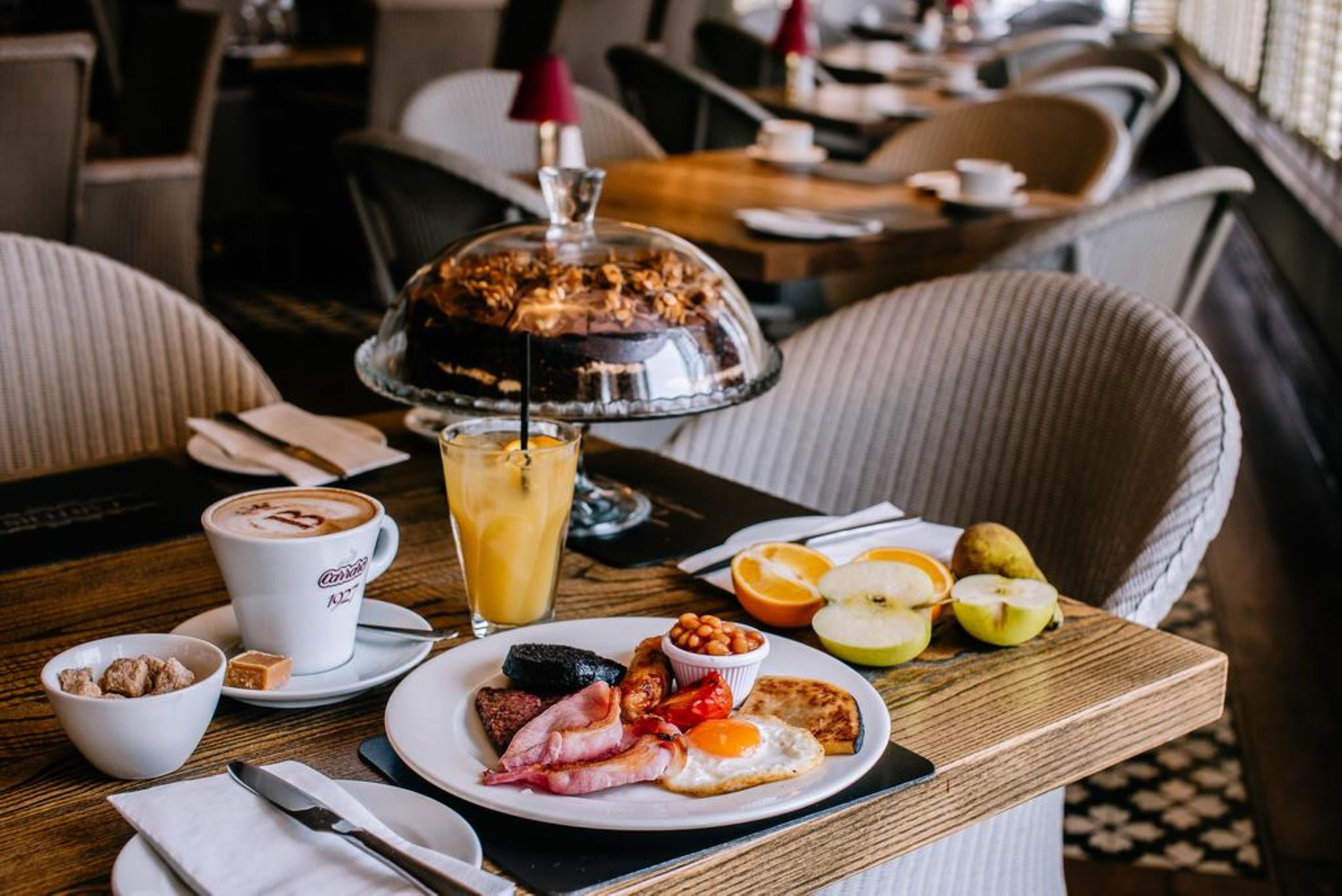 A breakfast setting with a plate of eggs, bacon, and toast, a coffee cup, and a fruit bowl.