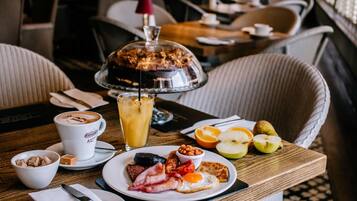 A breakfast setting with a plate of eggs, bacon, and toast, a coffee cup, and a fruit bowl.