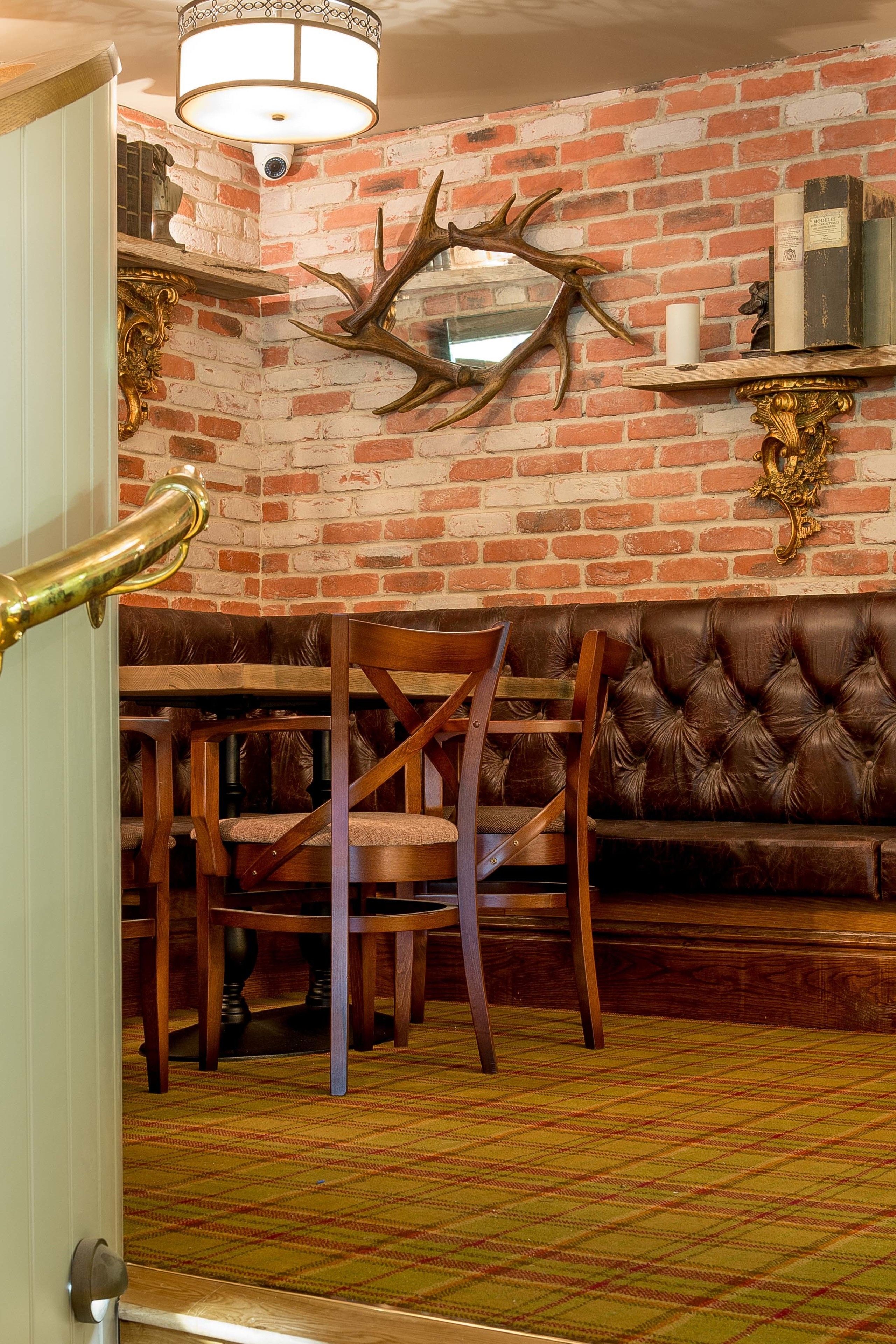 A room with a brick wall, a wooden dining table with chairs, a leather sofa, and a chandelier.