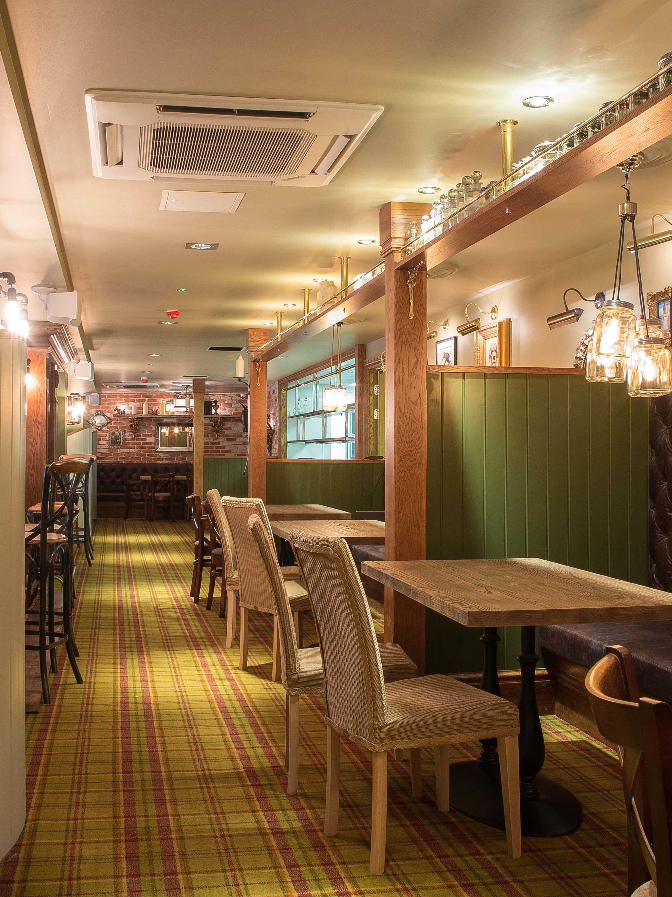 A restaurant interior with wooden tables and chairs, a checkered floor, and a bar area with shelves of bottles.