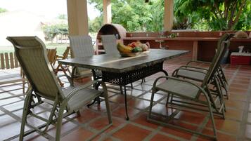A covered patio with a table and chairs, a grill, and a bowl of fruit.