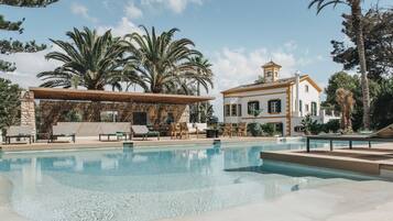 Relax by the serene pool surrounded by lush greenery and a Mediterranean-style building.