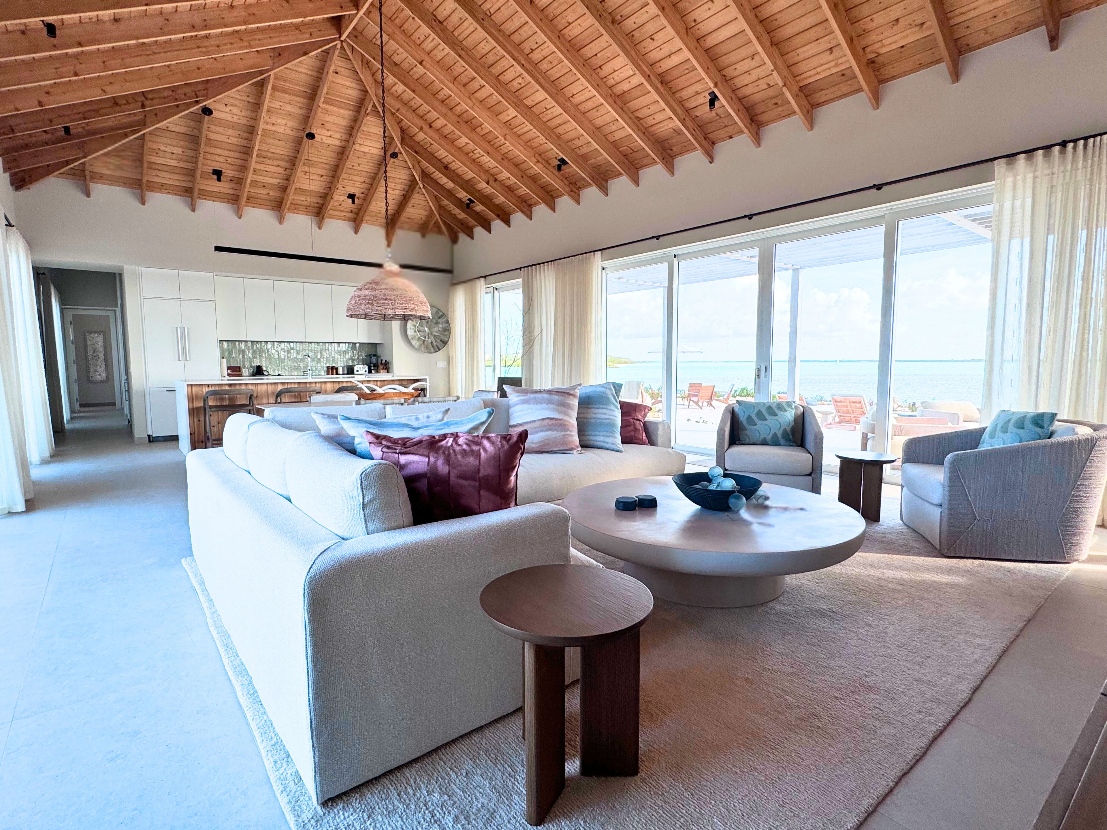Un amplio salón con techo alto, un conjunto de sofás, una mesa de centro y vistas al mar a través de amplias ventanas.