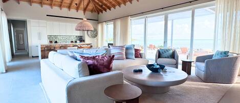 Un amplio salón con techo alto, un conjunto de sofás, una mesa de centro y vistas al mar a través de amplias ventanas.