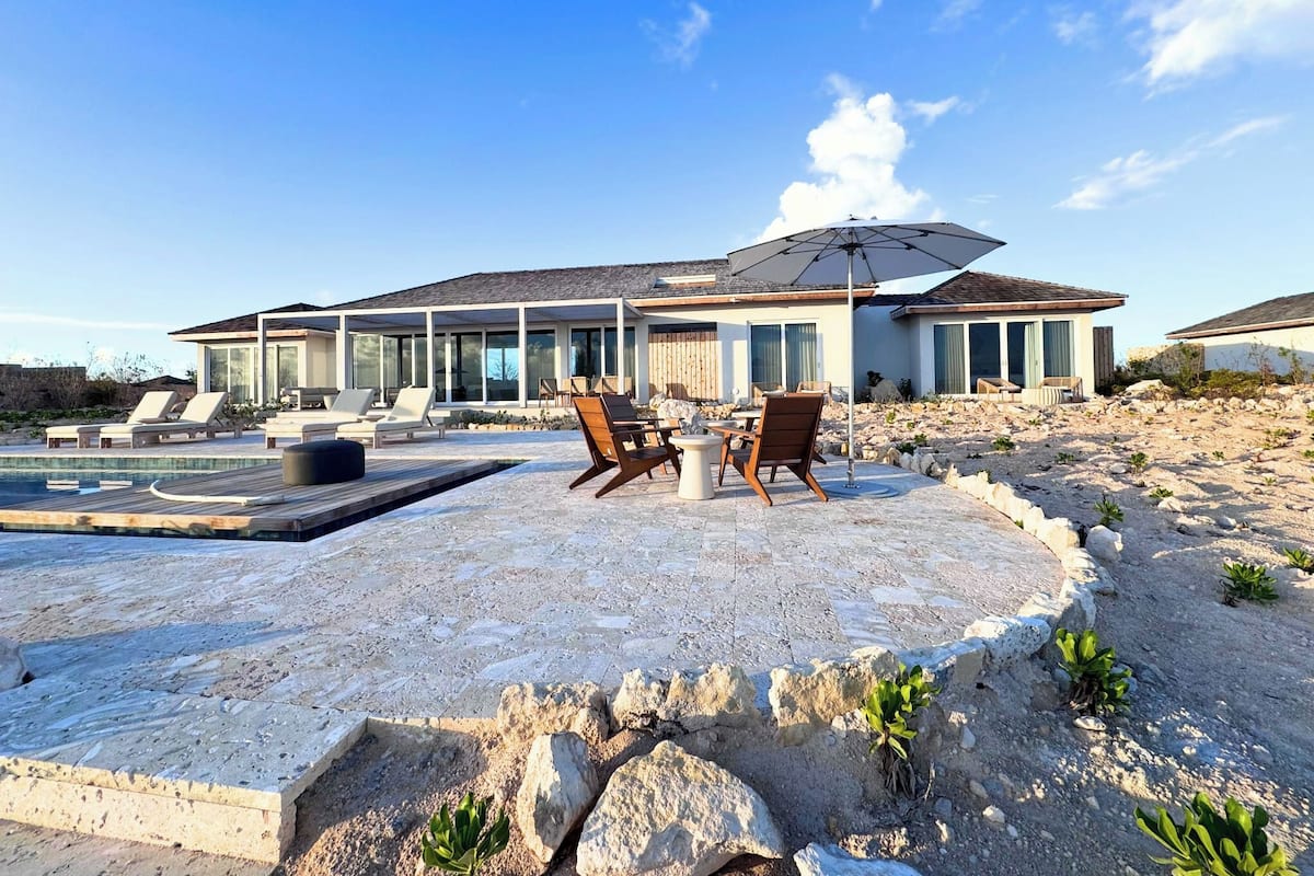 A modern house with a pool, outdoor seating, and a clear view of the surrounding landscape.