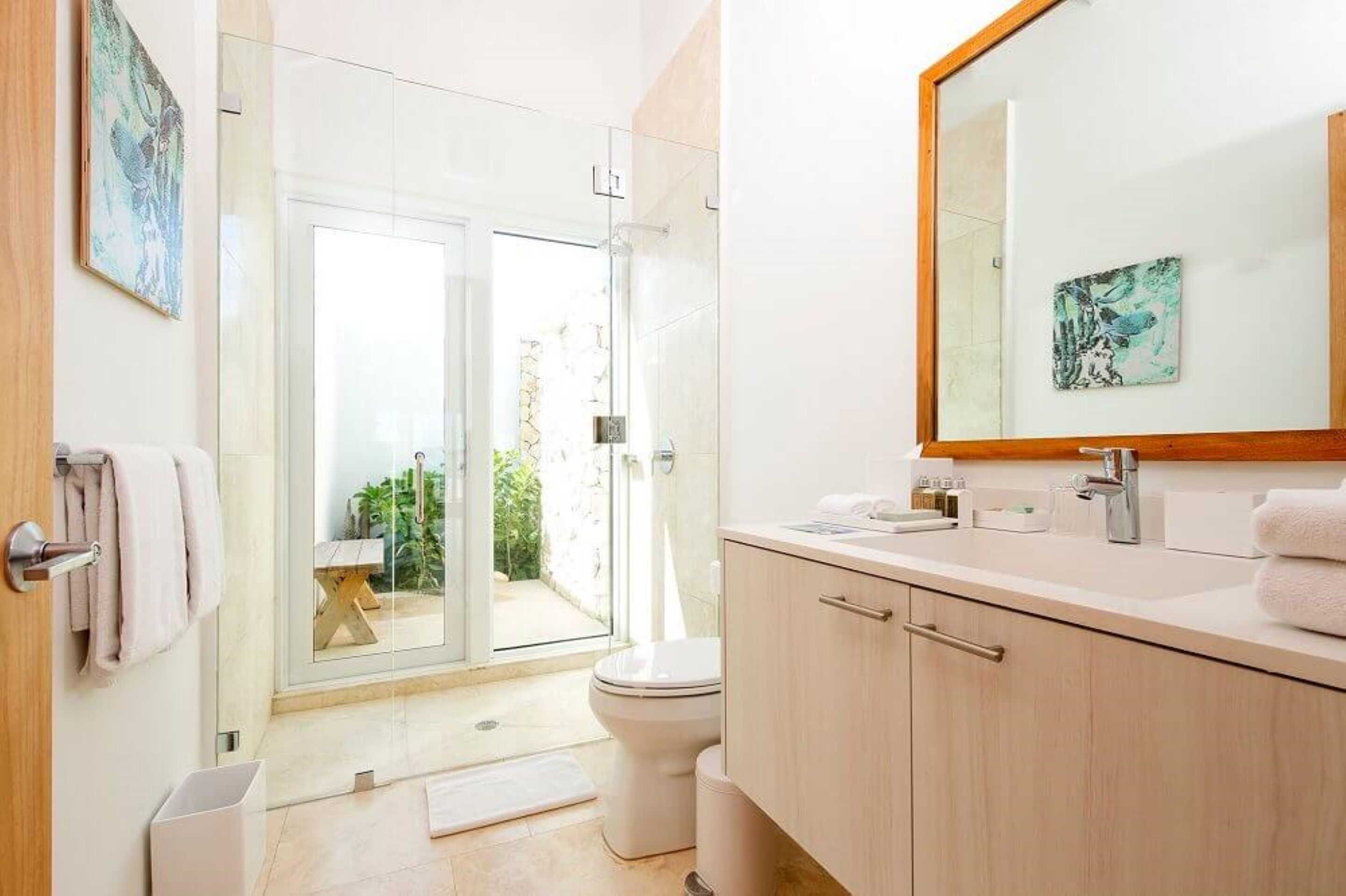 A modern bathroom with a glass door leading to a balcony, a sink with a mirror, and a toilet.