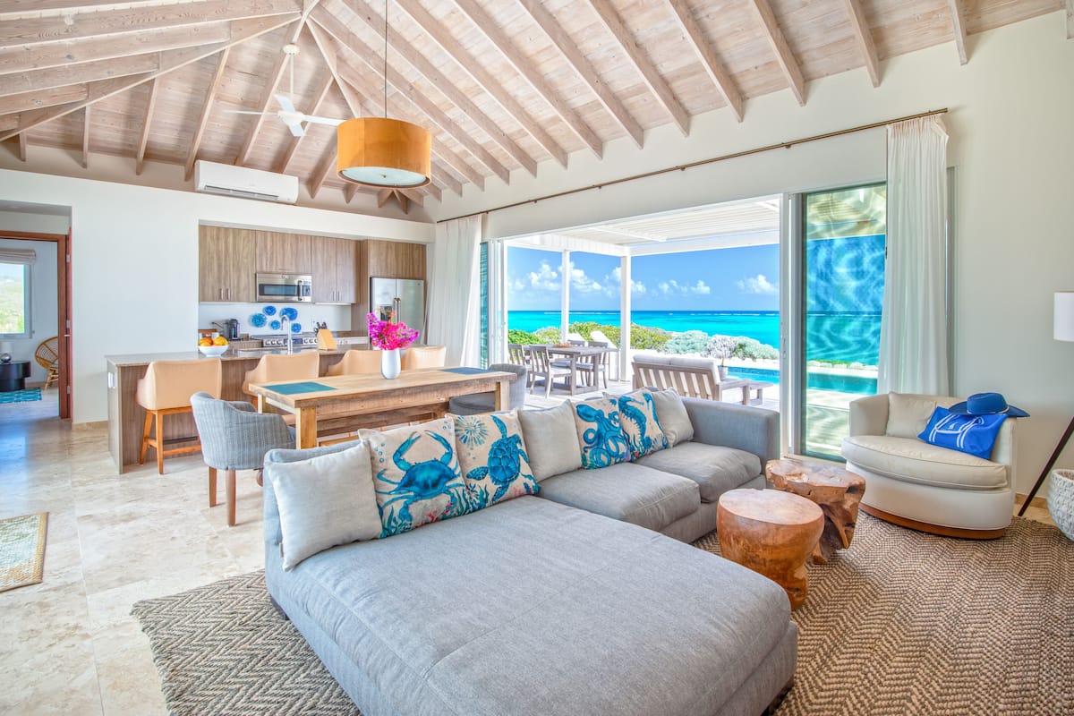 A spacious living area with a large gray sectional sofa, a wooden dining table, and a kitchen in the background.