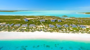 An aerial view of a coastal resort with multiple beachfront villas, clear turquoise waters, and lush greenery.
