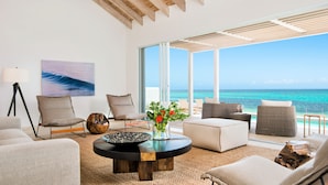 A modern living room with a large window overlooking the ocean, furnished with sofas, a coffee table, and a lamp.