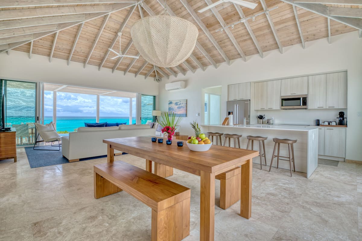 A spacious kitchen with a large island, wooden ceiling, and a view of the ocean.