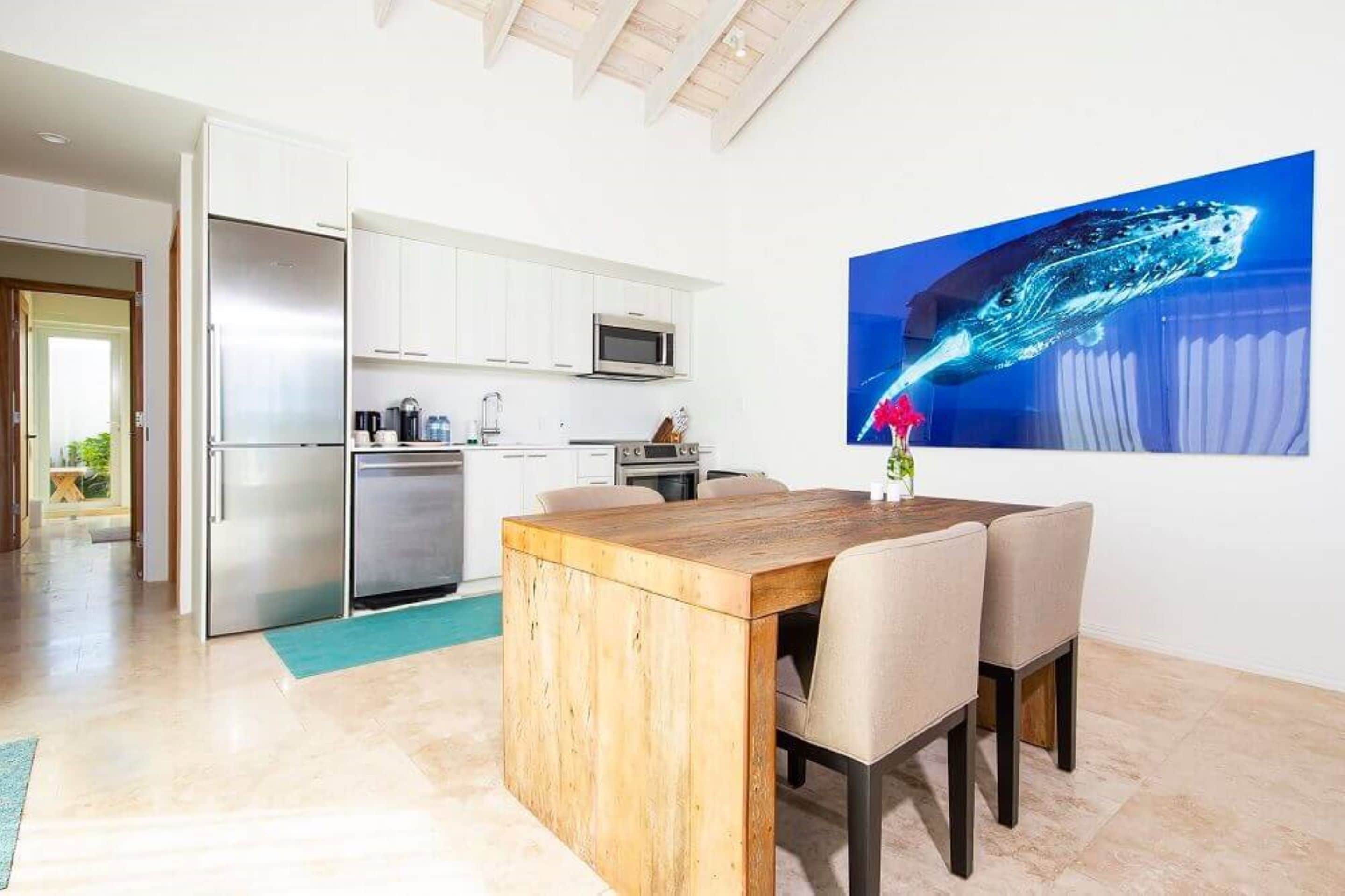 Una cocina moderna con armarios blancos, electrodomésticos de acero inoxidable y una mesa de comedor de madera con sillas.
