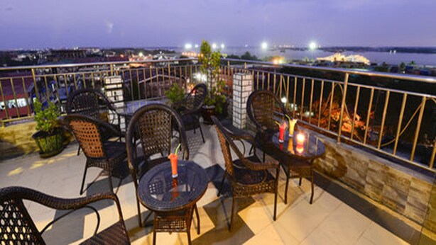 Una terraza al aire libre con mobiliario de mimbre, una pequeña mesa con velas y vistas a la ciudad al atardecer.