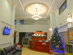 A lobby with a reception desk, a Christmas tree, a chandelier, and a television. - Millennium Hotel (Yangon)