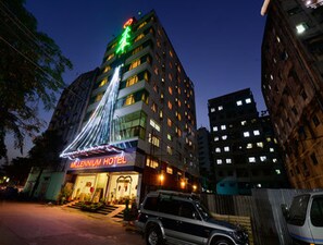 A hotel with a neon sign, a staircase leading to the entrance, and a vehicle parked in front. - Millennium Hotel (Yangon)