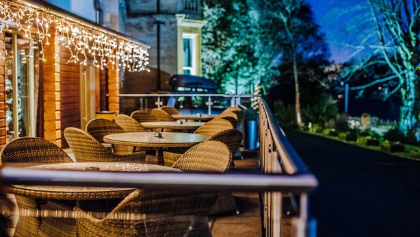 An outdoor seating area with wicker furniture and string lights. - The Lynnhurst Hotel (Johnstone)