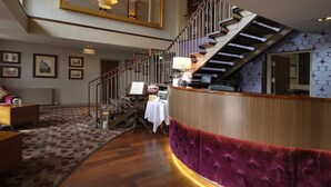 A hotel lobby with a wooden reception desk, a staircase, and a patterned carpet. - The Lynnhurst Hotel (Johnstone)
