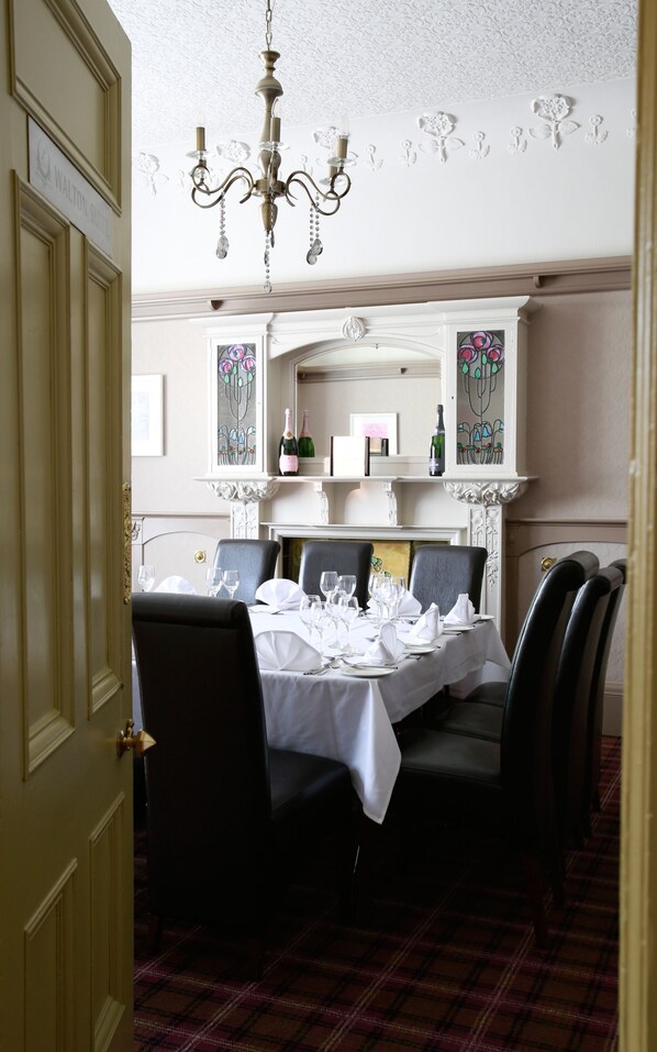 A dining room with a table set for four, a chandelier, and a fireplace. - The Lynnhurst Hotel (Johnstone)